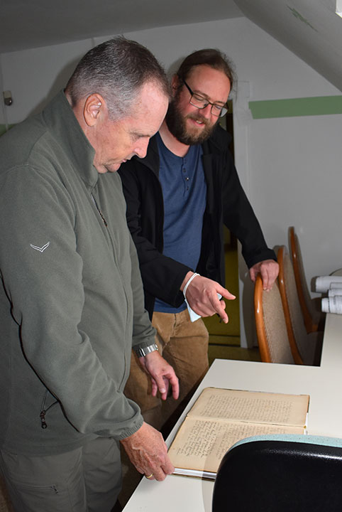 Zwei Männer unterhalten sich und blicken auf ein altes Papierdokument.