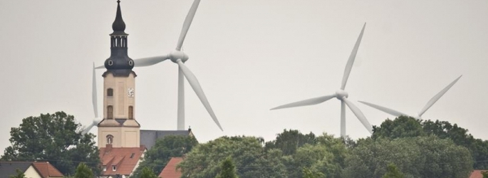 Windräder eines Windparks hinter dem Kirchturm einer Ortschaft